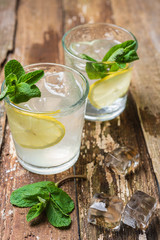 Two glasses of lemonade with with lemon slices, mint and ice on old wooden planks. Close up