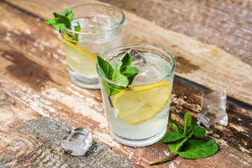 Two glasses of lemonade with with lemon slices, mint and ice on old wooden planks. Close up
