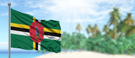 Waving Dominica flag in the sunny blue sky with summer beach background. Vacation theme, holiday concept.