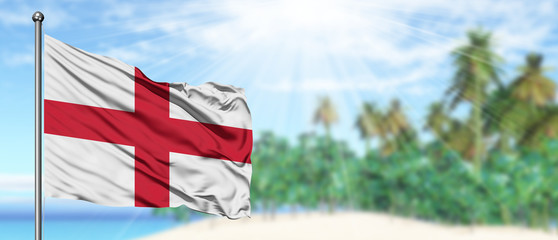 Waving England flag in the sunny blue sky with summer beach background. Vacation theme, holiday concept. © sezerozger
