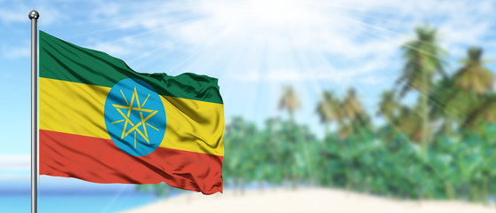 Waving Ethiopia flag in the sunny blue sky with summer beach background. Vacation theme, holiday concept.