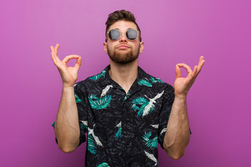 Young man wearing a vacation look relaxes after hard working day, he is performing yoga.