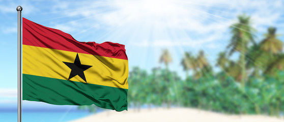 Waving Ghana flag in the sunny blue sky with summer beach background. Vacation theme, holiday concept.