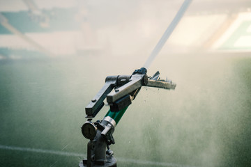 Automatic water irrigator in action. Close-up sprinkler of automatic watering. Green grass soccer field