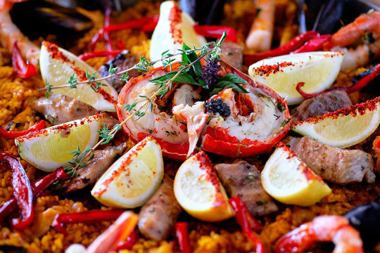 Close up above top view image of ripe ingredients of prepared served paella spanish traditional cuisine, bright colors. Dish garnished with lemon slices, lobster and aromatic herbs, Spain