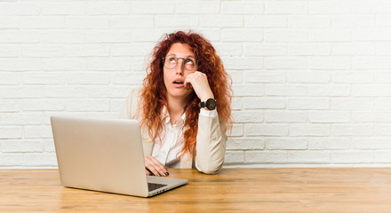 Young redhead curly woman working with her laptop tired of a repetitive task.