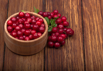 cowberries with leaves and wooden cup on wooden background