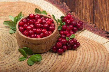 cowberries with leaves and wooden cup on wooden background