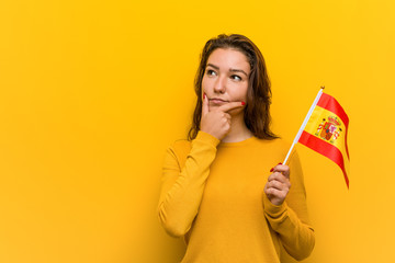 Young european woman holding a spanish flag looking sideways with doubtful and skeptical expression.