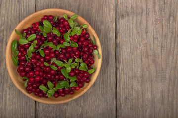 cowberries with green leaves in wooden cup on wooden background