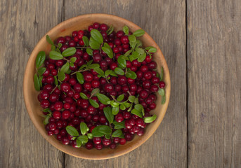 cowberries with green leaves in wooden cup on wooden background