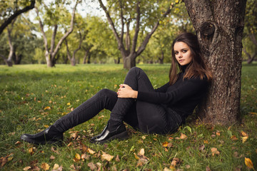 Obraz premium A beautiful young brunette walks through the autumn park in a black sweater and coat,