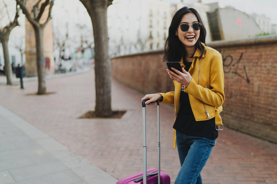 Young smiling woman traveler enjoying her first minutes in a new city and sharing the emotions with a friends online by a smartphone. Asian hipster girl reading messages on a mobile phone.