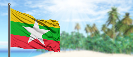 Waving Myanmar flag in the sunny blue sky with summer beach background. Vacation theme, holiday concept.