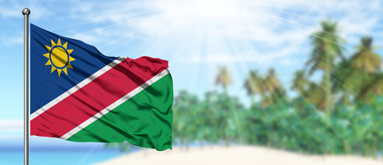 Waving Namibia flag in the sunny blue sky with summer beach background. Vacation theme, holiday...