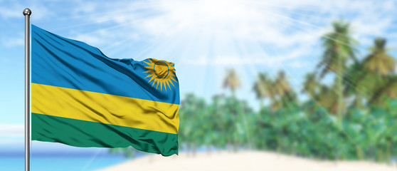 Waving Rwanda flag in the sunny blue sky with summer beach background. Vacation theme, holiday concept.