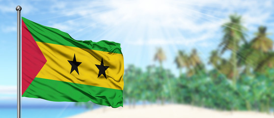 Waving Sao Tome And Principe flag in the sunny blue sky with summer beach background. Vacation theme, holiday concept.