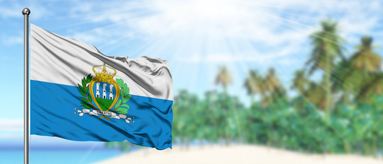 Waving San Marino flag in the sunny blue sky with summer beach background. Vacation theme, holiday concept.