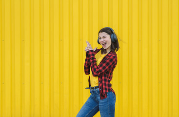 Happy girl listening to music on the street over yellow background