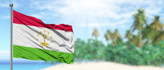 Waving Tajikistan flag in the sunny blue sky with summer beach background. Vacation theme, holiday concept.