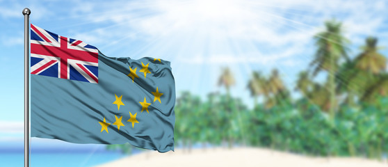 Waving Tuvalu flag in the sunny blue sky with summer beach background. Vacation theme, holiday concept.