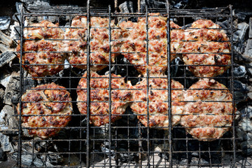 Meat patties are baked on a grill on a metal grill.