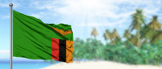 Waving Zambia flag in the sunny blue sky with summer beach background. Vacation theme, holiday concept.