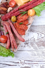 Smoked sausages assortment, cheese, nuts, cherry tomatoes, pickled vegetables and olives on the white wooden table. Varied appetizers. Top view