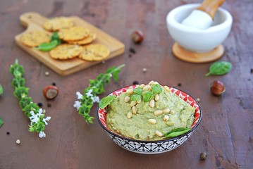 Green pea spread with almonds and basil on a brown concrete background. Decorated with pine nuts, served with crackers.