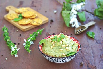 Green pea spread with almonds and basil on a brown concrete background. Decorated with pine nuts, served with crackers.