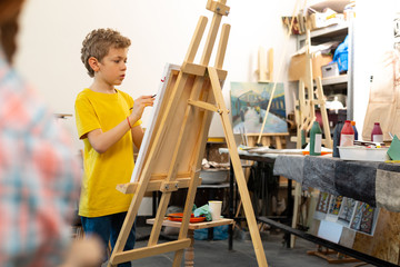 Boy wearing yellow t-shirt painting on drawing easel