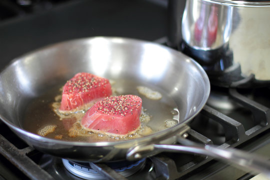 Ahi tuna steaks searing in a stainless steel pan on a gas stove.