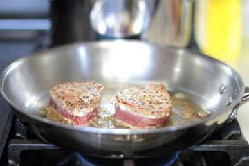 Ahi tuna steaks searing in a stainless steel pan on a gas stove.
