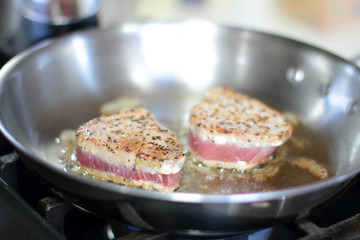 Ahi tuna steaks searing in a stainless steel pan on a gas stove.