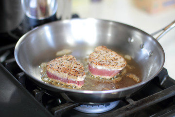 Ahi tuna steaks searing in a stainless steel pan on a gas stove.