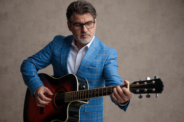 Focused businessman playing acoustic guitar while wearing a blue suit