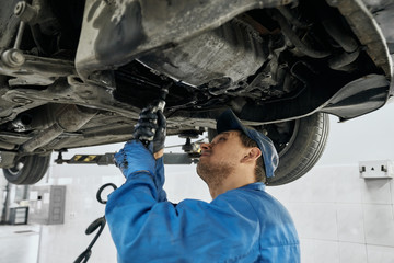 Professional mechanic working with tools under lifted car