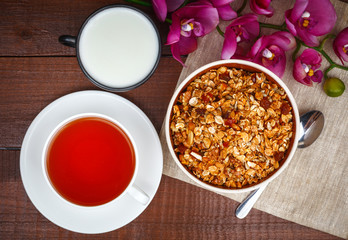 Granola with milk in bowl and cup of tea