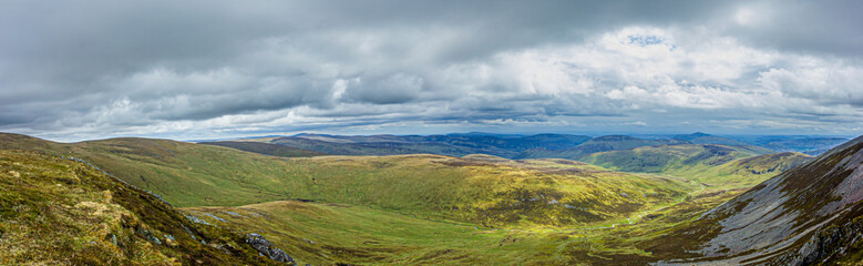 A panorama view of a Scottish mountain valley with heather and stream under a stormy huge white clouds sky