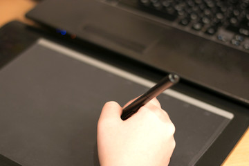 Female hand working on a black, graphic tablet. At the brown table