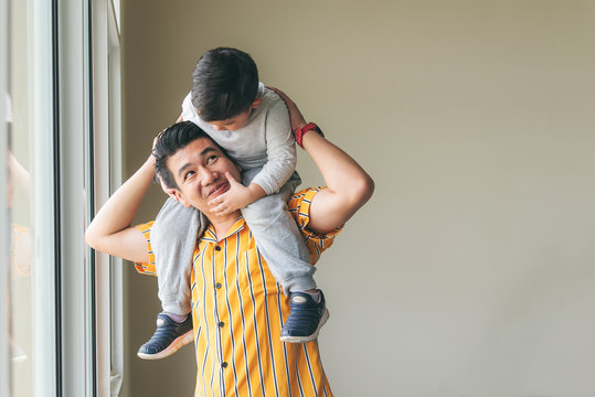 Cute son riding his father's throat standing by the window, Are happy to family concept.