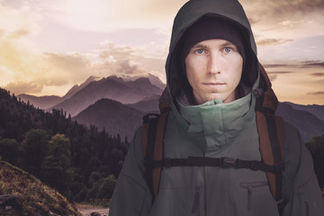 Young male hiker on cloudy mountain landscape background looking at camera. Front view. Active lifestyle and tourism.