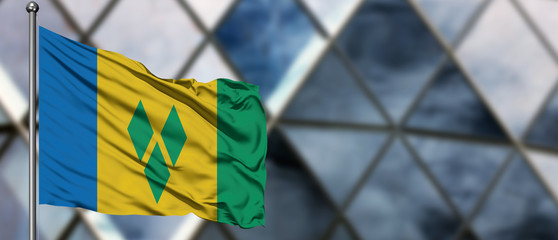 Saint Vincent And The Grenadines flag waving in the wind against blurred modern building. Business concept. National cooperation theme.