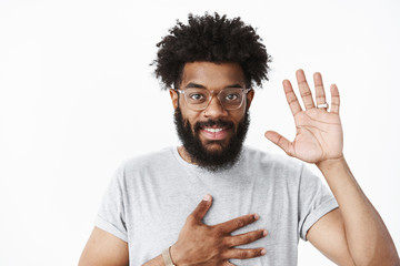 Friendly nice african american man at meeting holding palm on chest and raising hand in hello,...