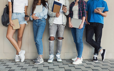 Teenagers standing at campus wall, holding devices and books