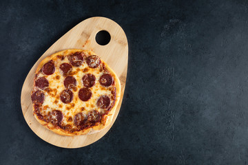 Top view of pepperoni pizza on black concrete background. Copy space for text.