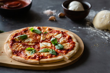 Ingredients for traditional Italian pizza Margherita with tomato sauce, Mozzarella cheese, basil on a dark concrete background. Pizza recipe and menu.