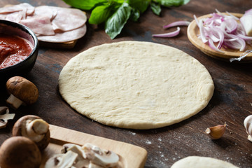 Top view of raw dough, ingredients and spices for pizza with ham and mushrooms on wooden background.