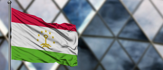 Tajikistan flag waving in the wind against blurred modern building. Business concept. National cooperation theme.