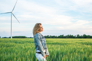 Naklejka na ściany i meble young attractive female on the field of wheat near a wind turbine generators, sunset orange light